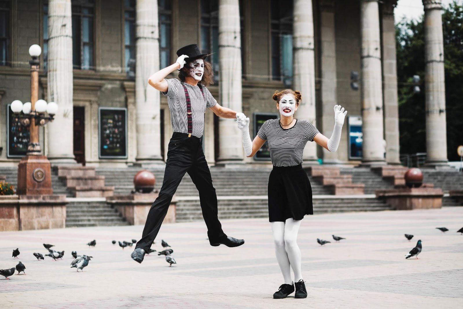 Street mime performers in striped shirts and white face paint entertaining in public square with pigeons in London.