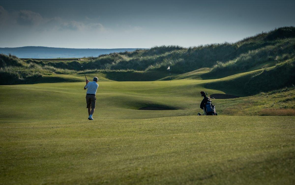Golfer taking a swing on a windswept links course, embodying the raw beauty and challenge of Scotland golfing along the coast.