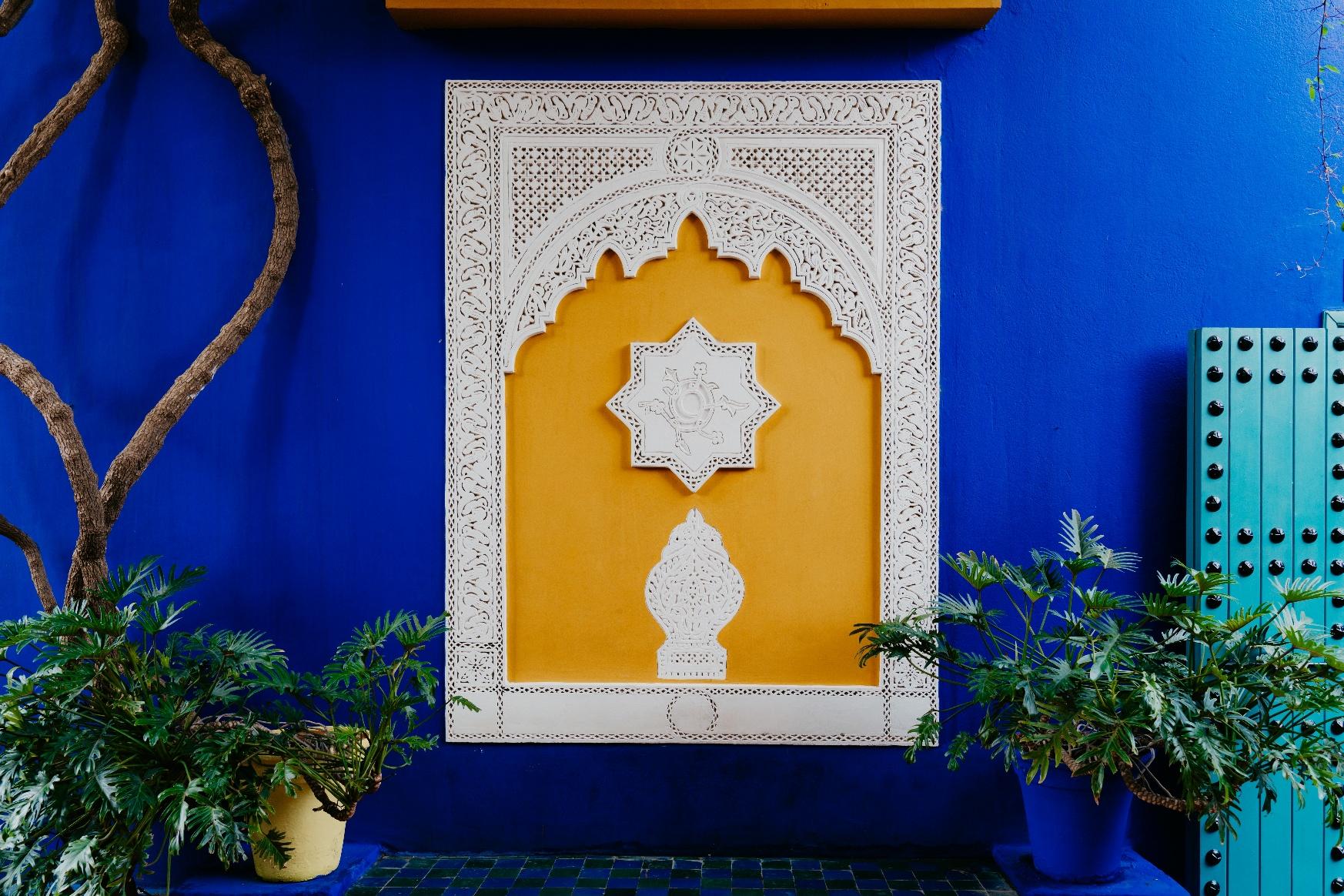 Vibrant blue and yellow architectural detail in a luxury garden in Morocco, featuring intricate Islamic design and lush greenery.